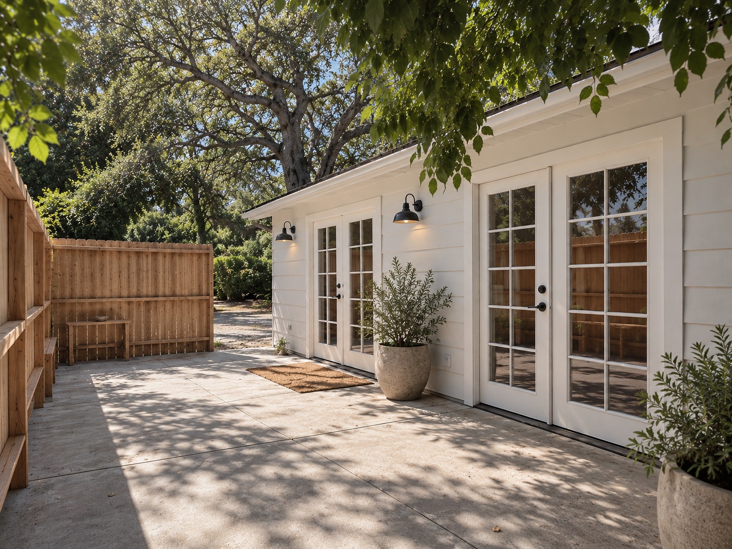ADU exterior with white siding, French doors and a sunny paved patio