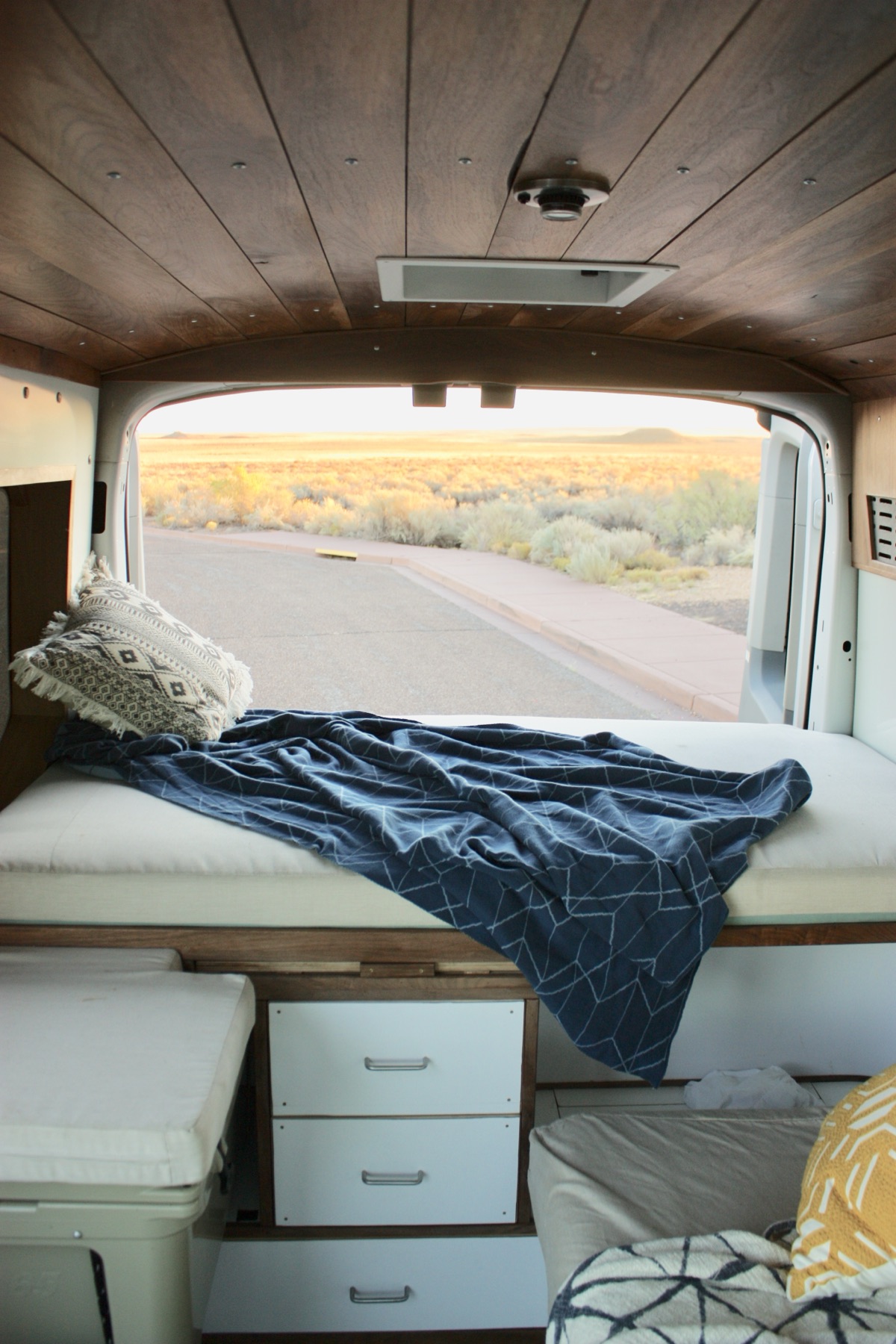 Converted van interior with a bed, white built-in drawers and a view out the open back doors